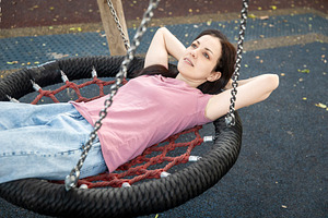 Woman relaxing on a nest swing at a playground, looking up towar, a Person Photo by Imaginarium