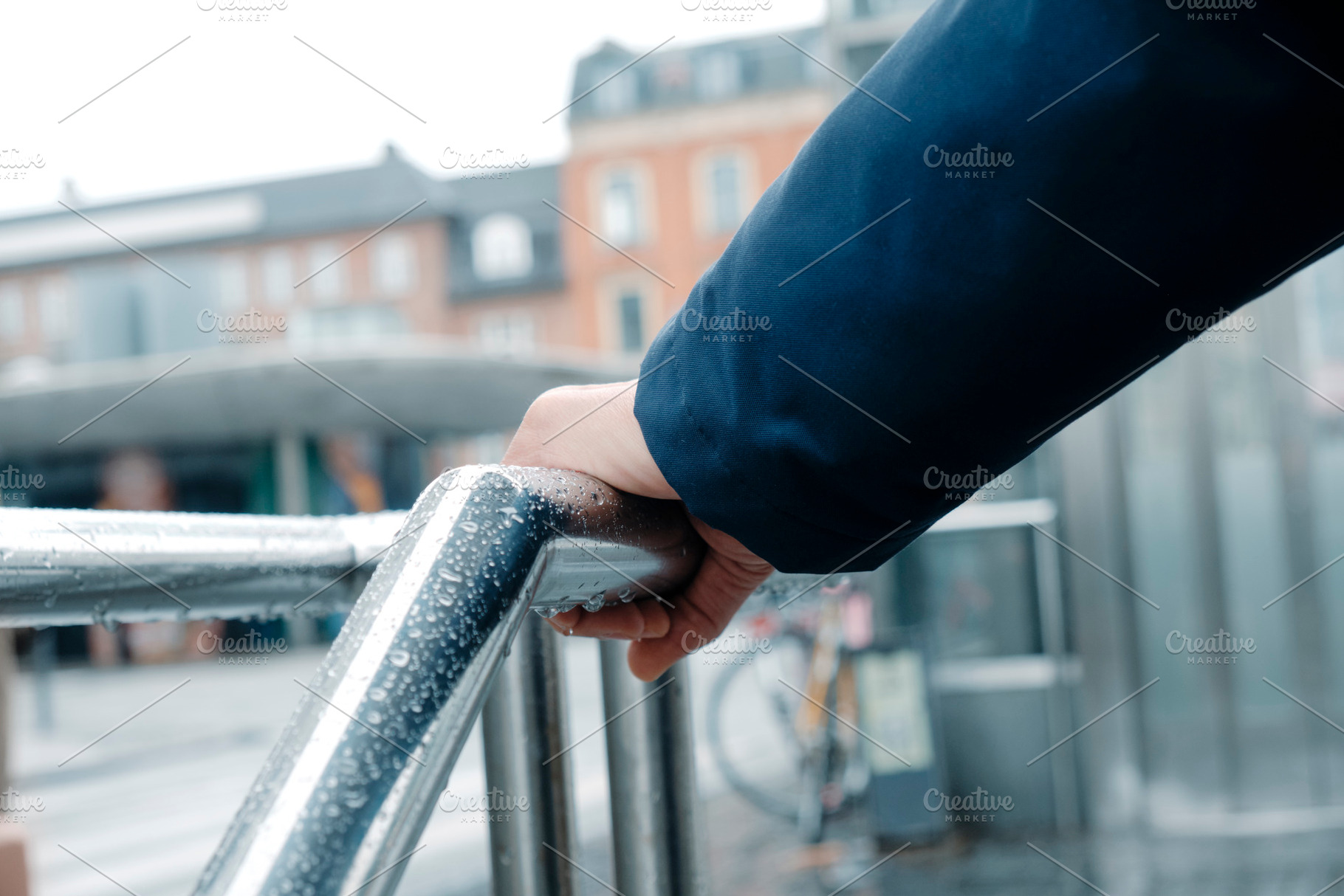 a man grips a rain-covered railing in Copenhagen, a Photo by Nito