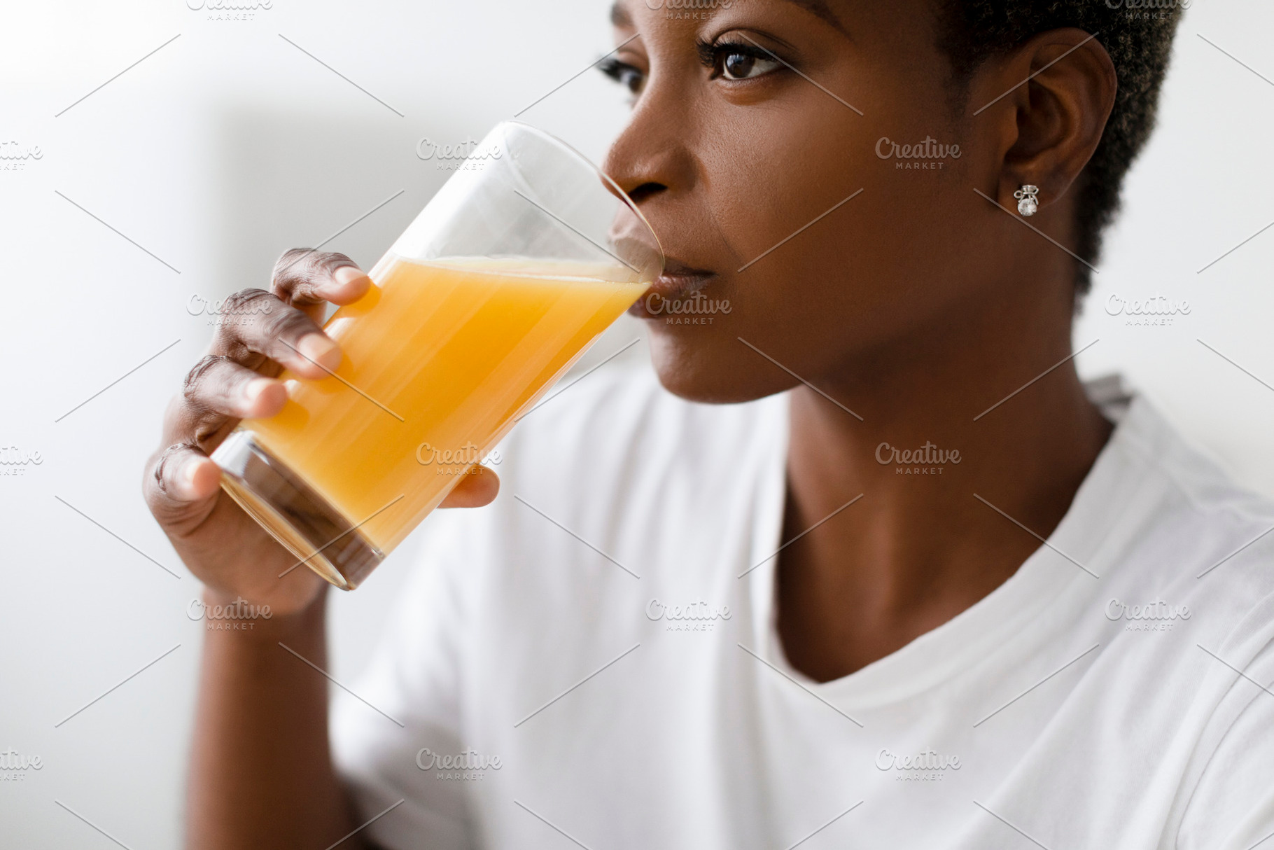 Cropped thirsty young pretty black lady in white t-shirt drinks fresh orange ju, a Person Photo by Prostock-Studio