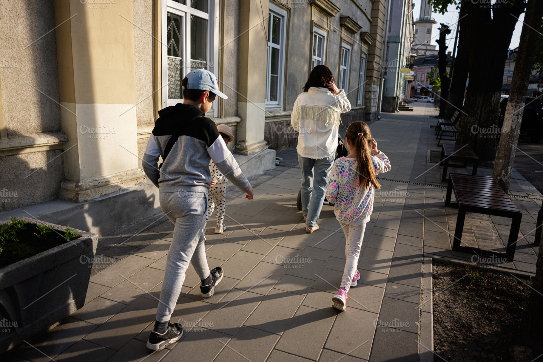 Family walks together along a sunny city sidewalk by residential buildings, a Person Photo by AS photostudio
