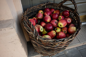 Wicker basket filled with ripe red apples placed near a rustic doorway, a Photo by AS photostudio