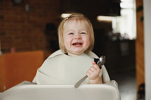 Infant girl or toddler sitting on high chair. Eating food by herself using spoo, a Person Photo by Lenor4ik