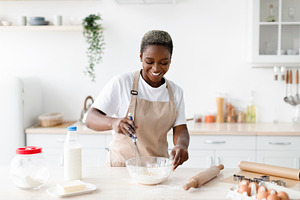 Glad happy young african american female in apron make dough for baking, prepar, a Person Photo by Prostock-Studio