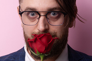 Bearded man in glasses holding red rose in front of face, wearin, a Person Photo by Ales Munt