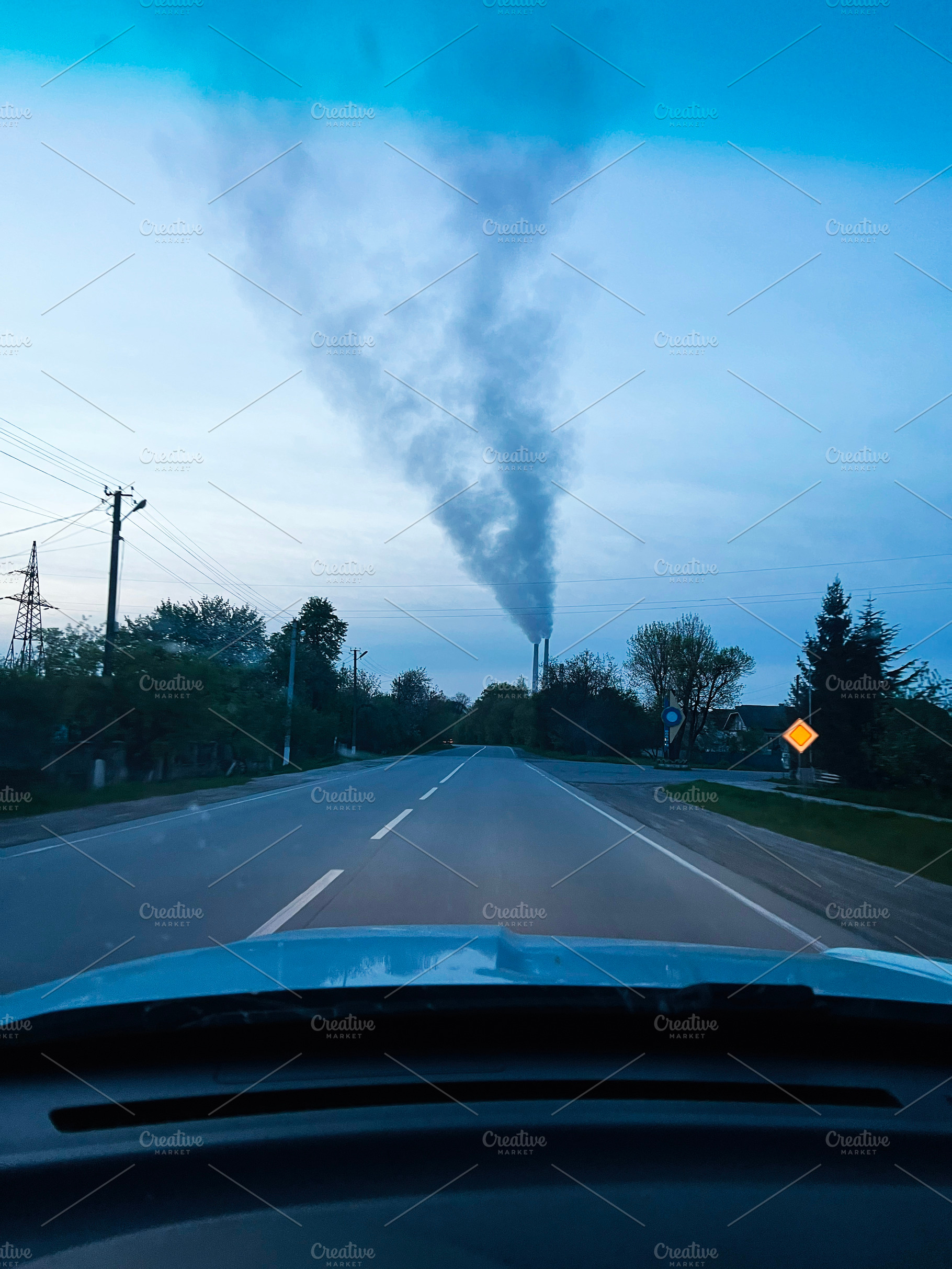 Empty rural road with TPP smoke rising into sky from distant chimney, a Photo by AS photostudio
