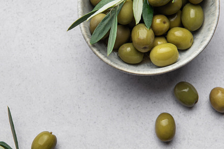Green olives with leaves served in bowl on concrete table, creat, a Food & Drink Photo by Olena Rudo