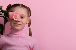 Cheerful young girl holding a pink rose in front of her eye, aga, a Person Photo by Ales Munt