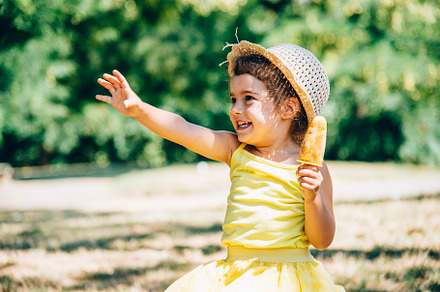 Cute happy little girl in yellow dress and hat eating fruit ice, a Person Photo by hitdelight