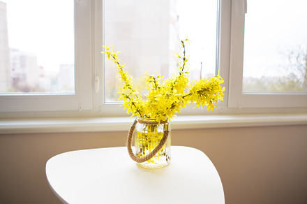 A bouquet of yellow flowers in a vase stand on a white table, a Nature Photo by Artsaba Family