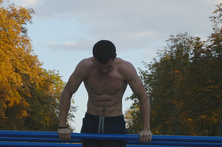 Athletic man doing push ups on parallel bars at sports ground in city park, a Sports & Recreation Photo by Footage Autor
