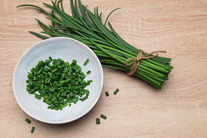 Fresh chives bundle and chopped pieces on wooden surface, a Food & Drink Photo by Olena Rudo