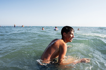 Teenage boy enjoying a sunny day swimming in the ocean with others in the backg, a Photo by AS photostudio