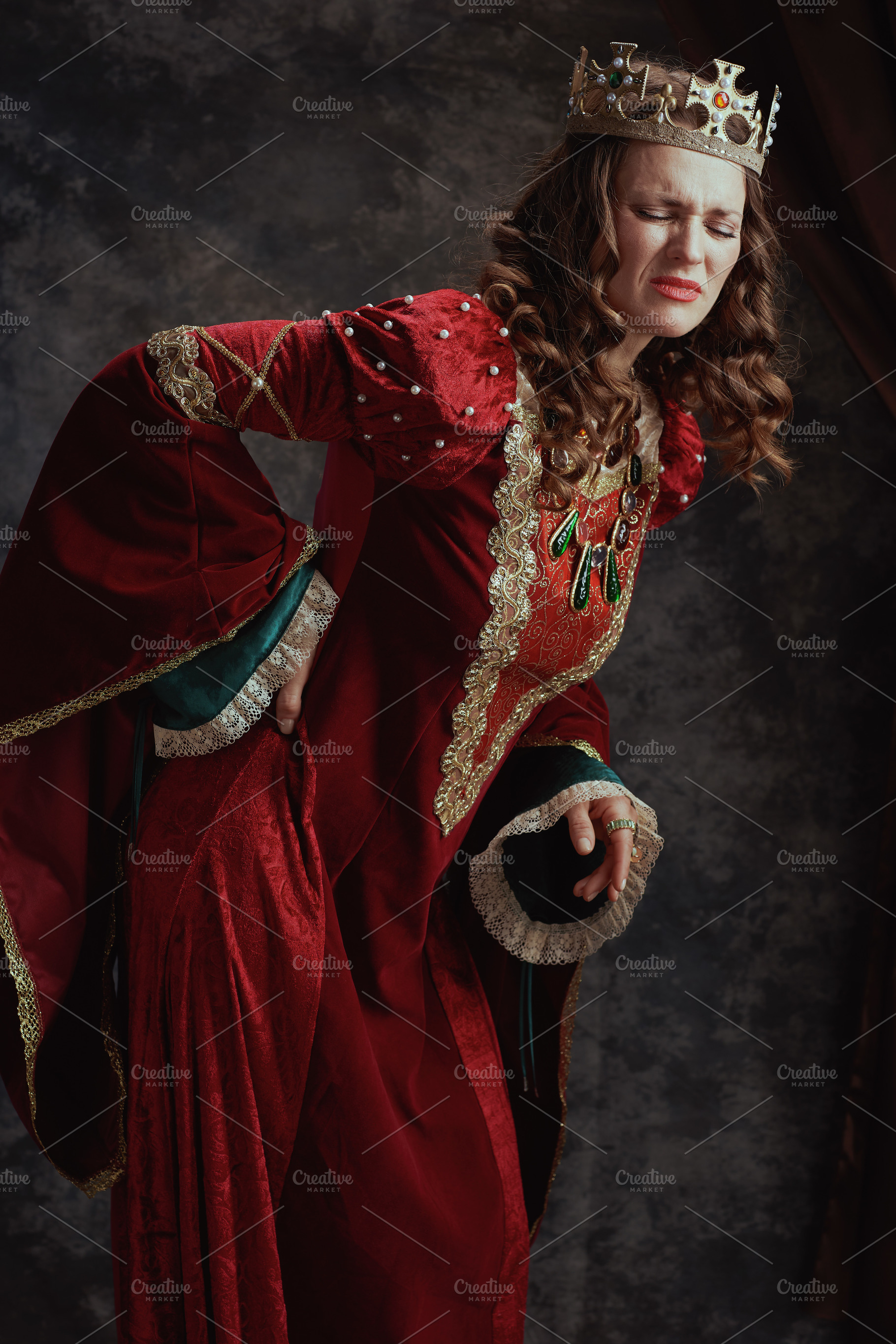 tired medieval queen in red dress with crown having backache, a Person Photo by Alliance Images