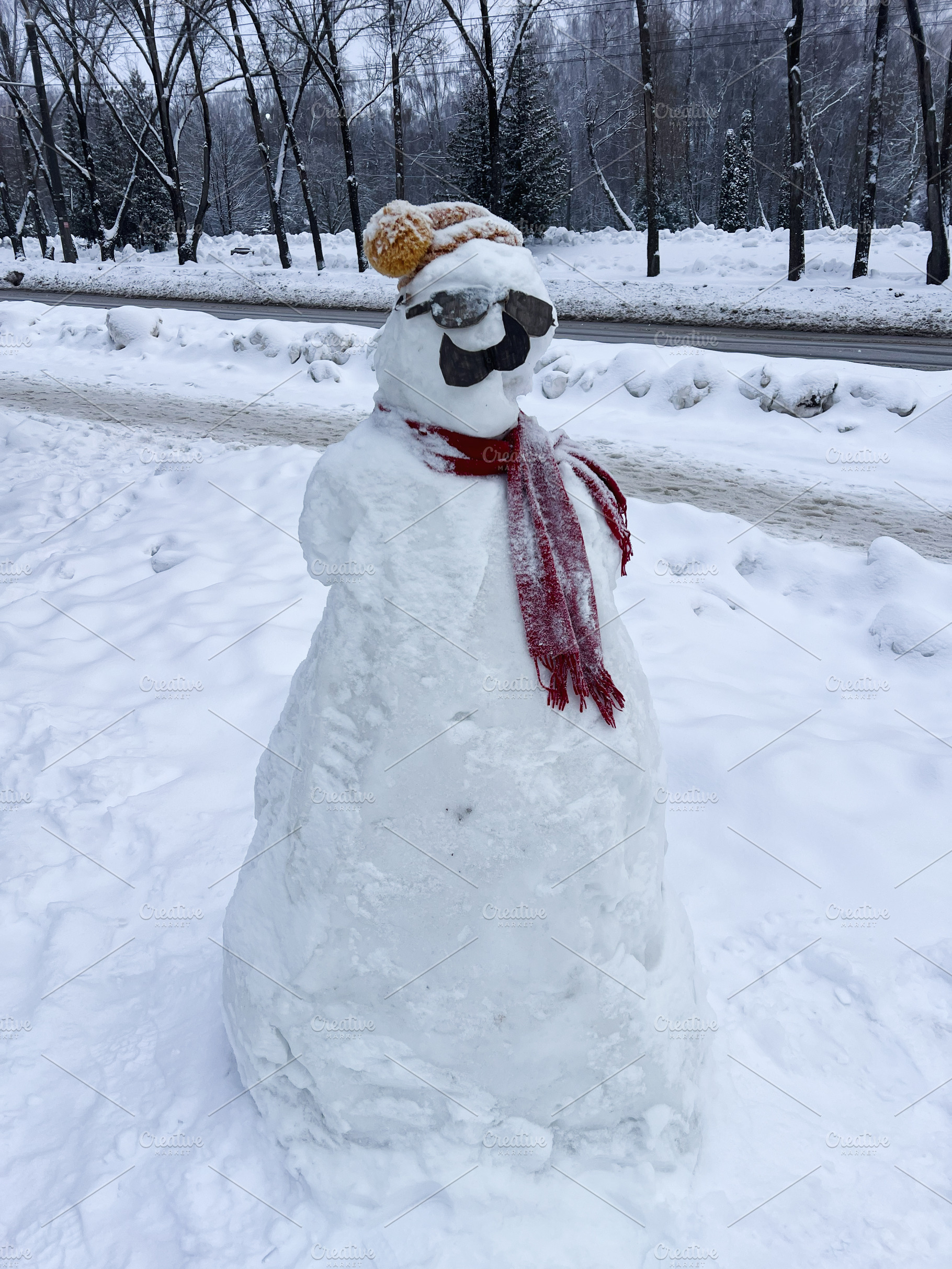 Snowman wearing scarf and sunglasses in snowy park on a chilly winter day, a Photo by AS photostudio
