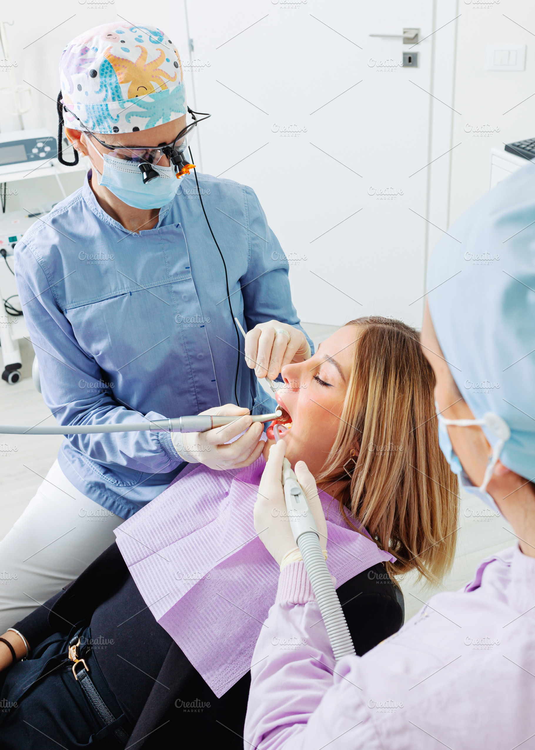 Dentist and assistant performing dental checkup on female patient, a Health & Medical Photo by Antonio Gravante Market