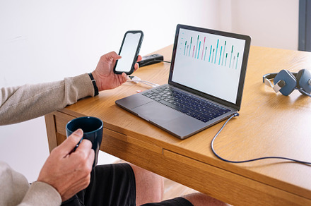 Man working from home on a laptop and smart phone sitting at a desk surfing the, a Person Photo by karrastock