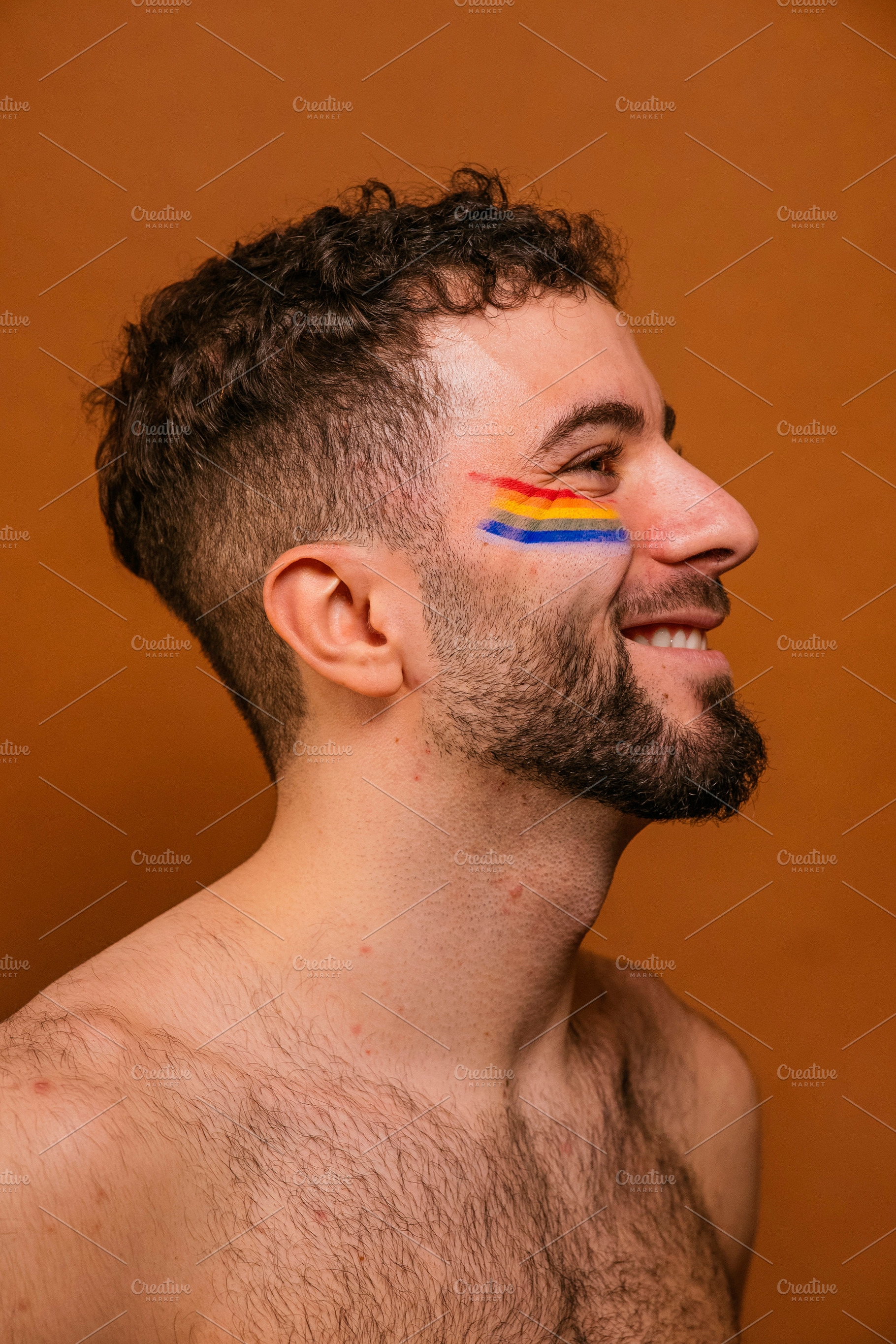 Smiling man celebrating pride with rainbow face paint, a Photo by karrastock