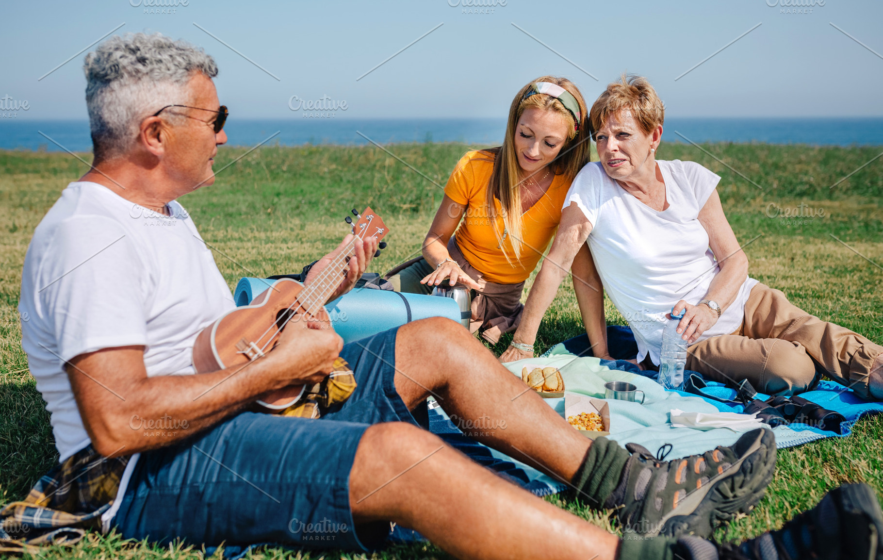 Senior man playing ukulele for his family sitting on a blanket during an excurs, a Holiday Photo by davidpereiras