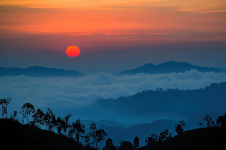 The sun sets behind rolling mountain, a Photo by Tanuart
