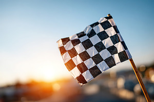 Checkered race flag waving on a wooden pole at sunset during an outdoor racing, an Arts & Entertainment Photo by AlyaAnd