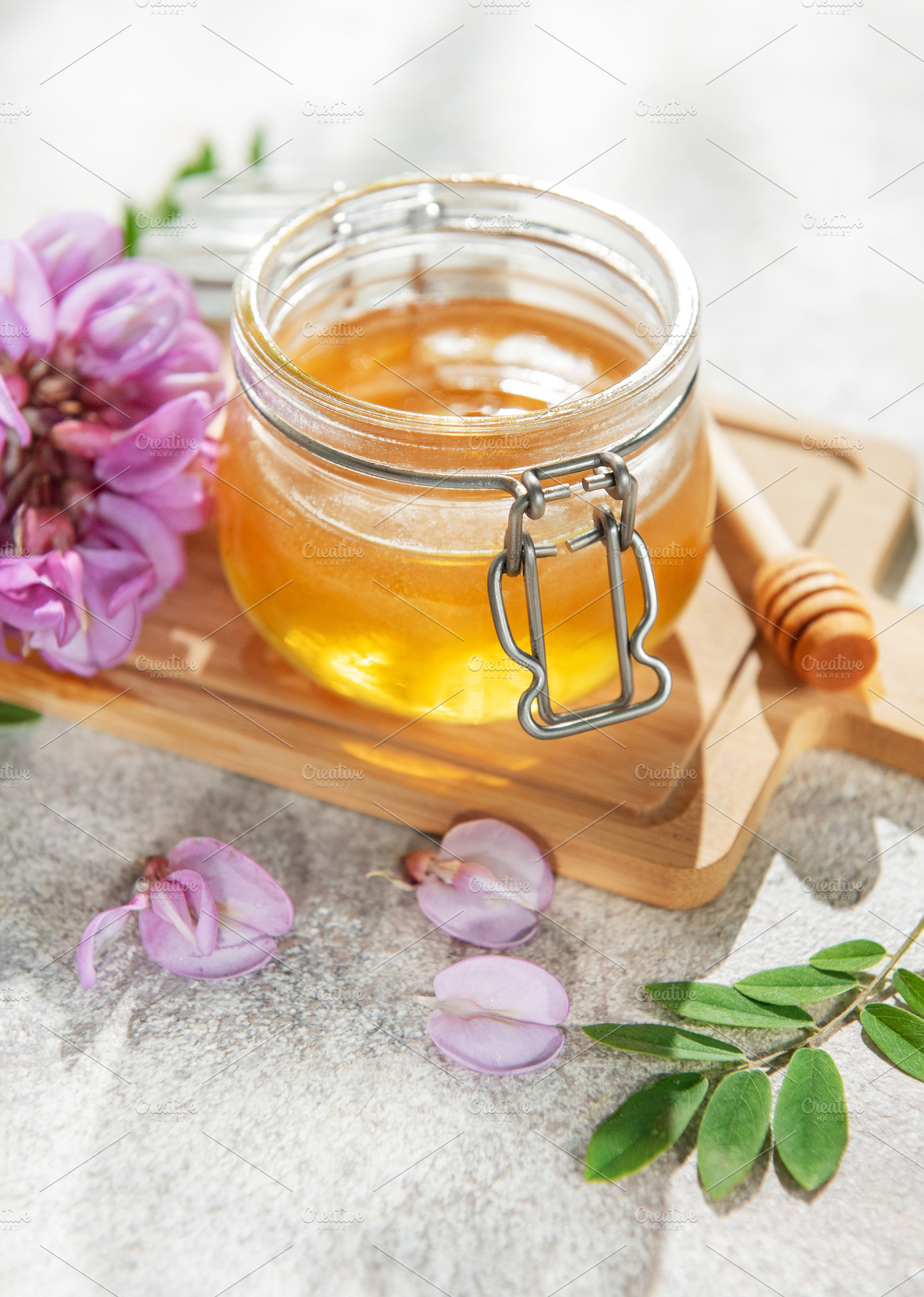 Acacia honey jar with blooming flowers and wooden dipper, a Food & Drink Photo by Olena Rudo
