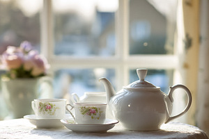 Teapot, tea cups, and saucers arranged on a table in front of a, a Photo by Studio ANNA
