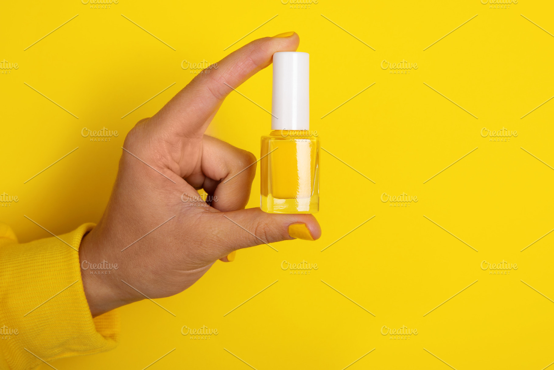 Close-up of a hand holding a yellow nail polish bottle against a, a Photo by Ales Munt