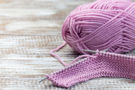 Piece of knitting with needles and pink yarn skein on wooden background, horizo, an Arts & Entertainment Photo by iuliia_n