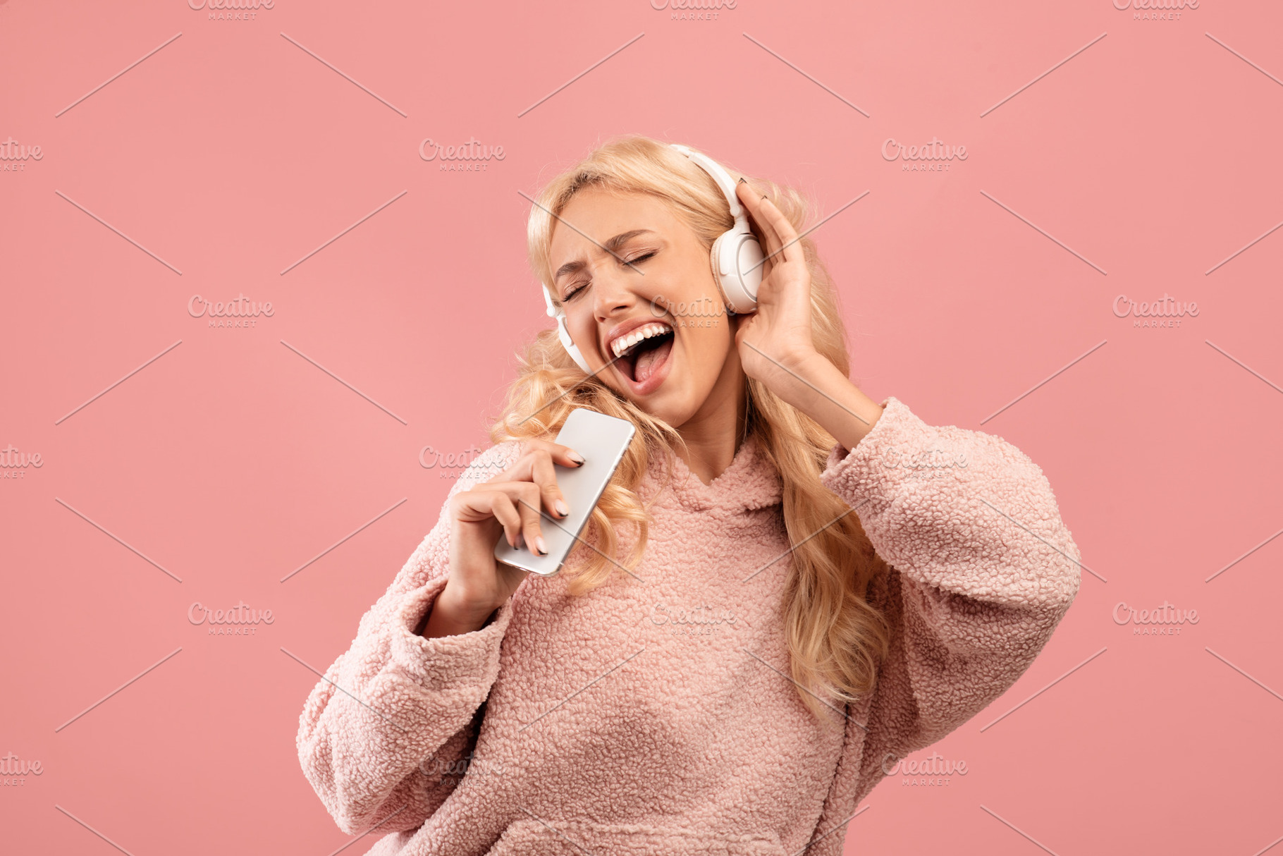 Playful young lady singing and holding smartphone like microphone wearing wirel, a Photo by Prostock-Studio