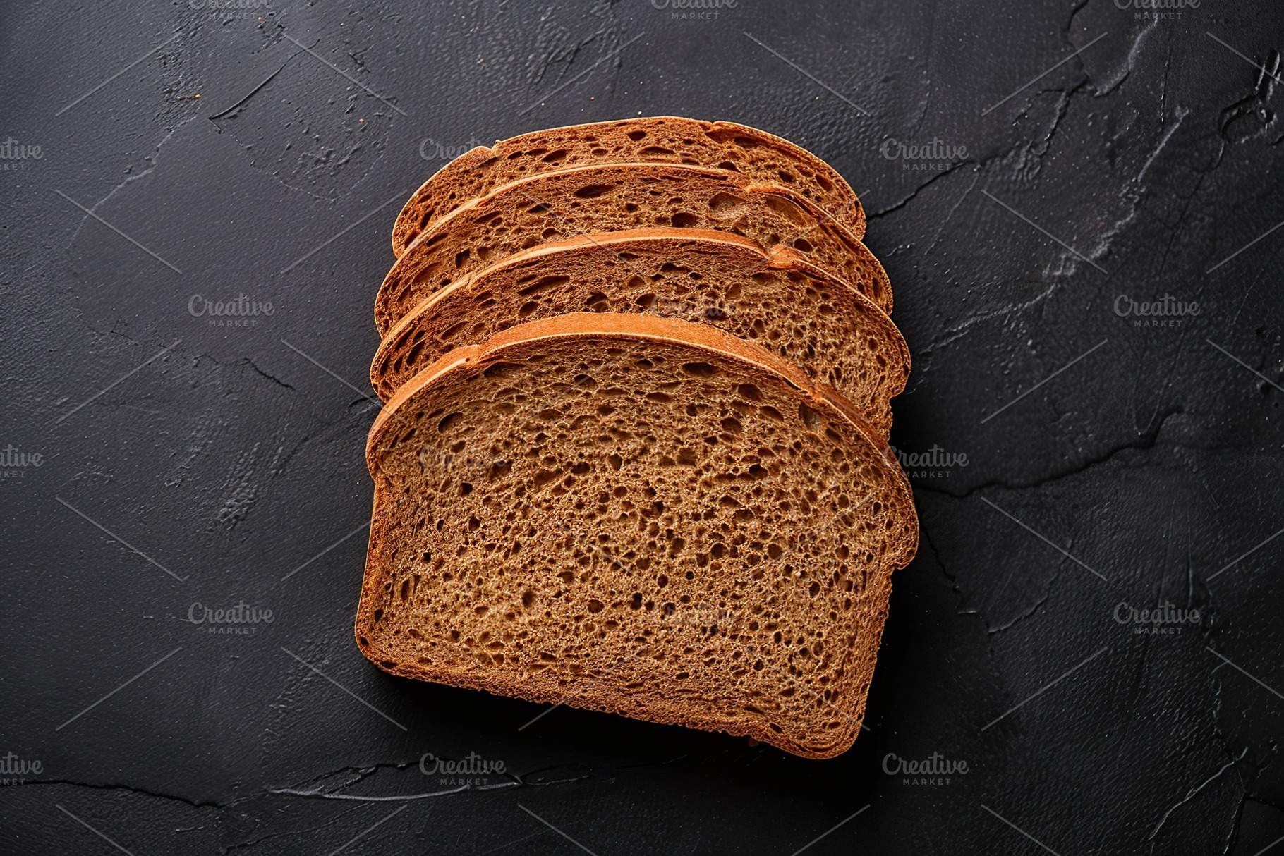 Sliced baked rye bread on black background, a Food & Drink Photo by AlyaAnd