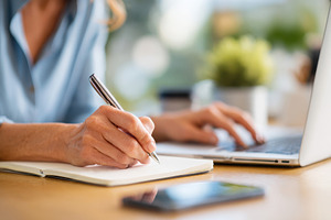 Person writing in notebook while using laptop, a Business Photo by AlyaAnd