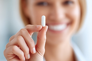 Smiling woman holds a white capsule, a Health & Medical Photo by MistyDay