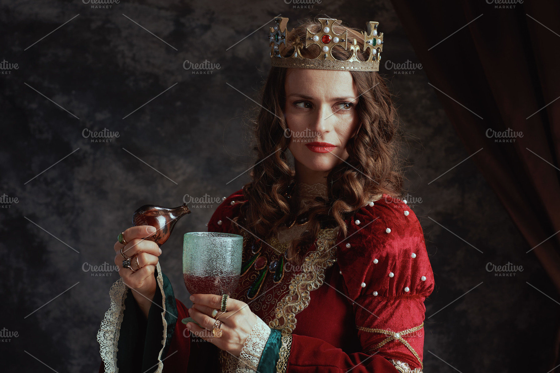 pensive medieval queen in red dress pouring poison into goblet, a Person Photo by Alliance Images