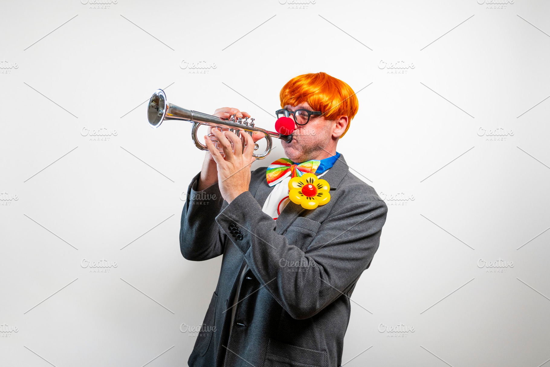 Clown playing trumpet with bright orange wig and red nose, a Person Photo by karrastock