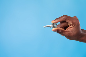 Unrecognizable young black man holding metal house key on blue studio backgroun, a Photo by Prostock-Studio