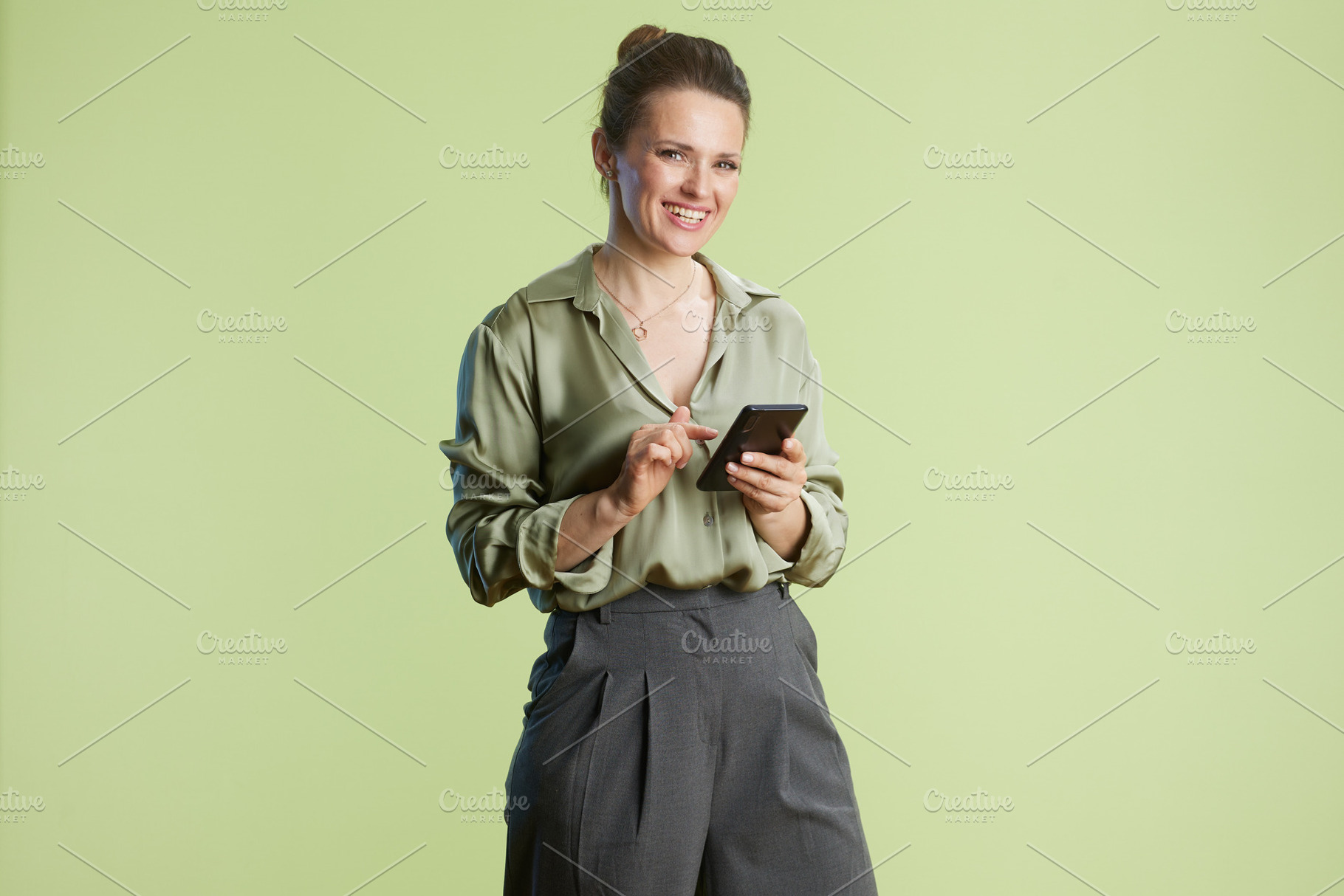 Smiling woman with smartphone against green backdrop, a Person Photo by Alliance Images