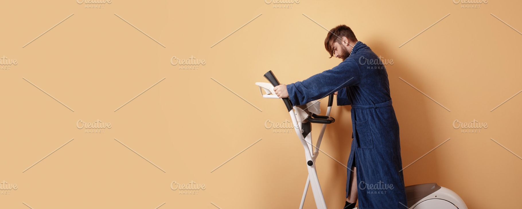 Young man using stationary bike in blue bathrobe against pastel, a Person Photo by Ales Munt