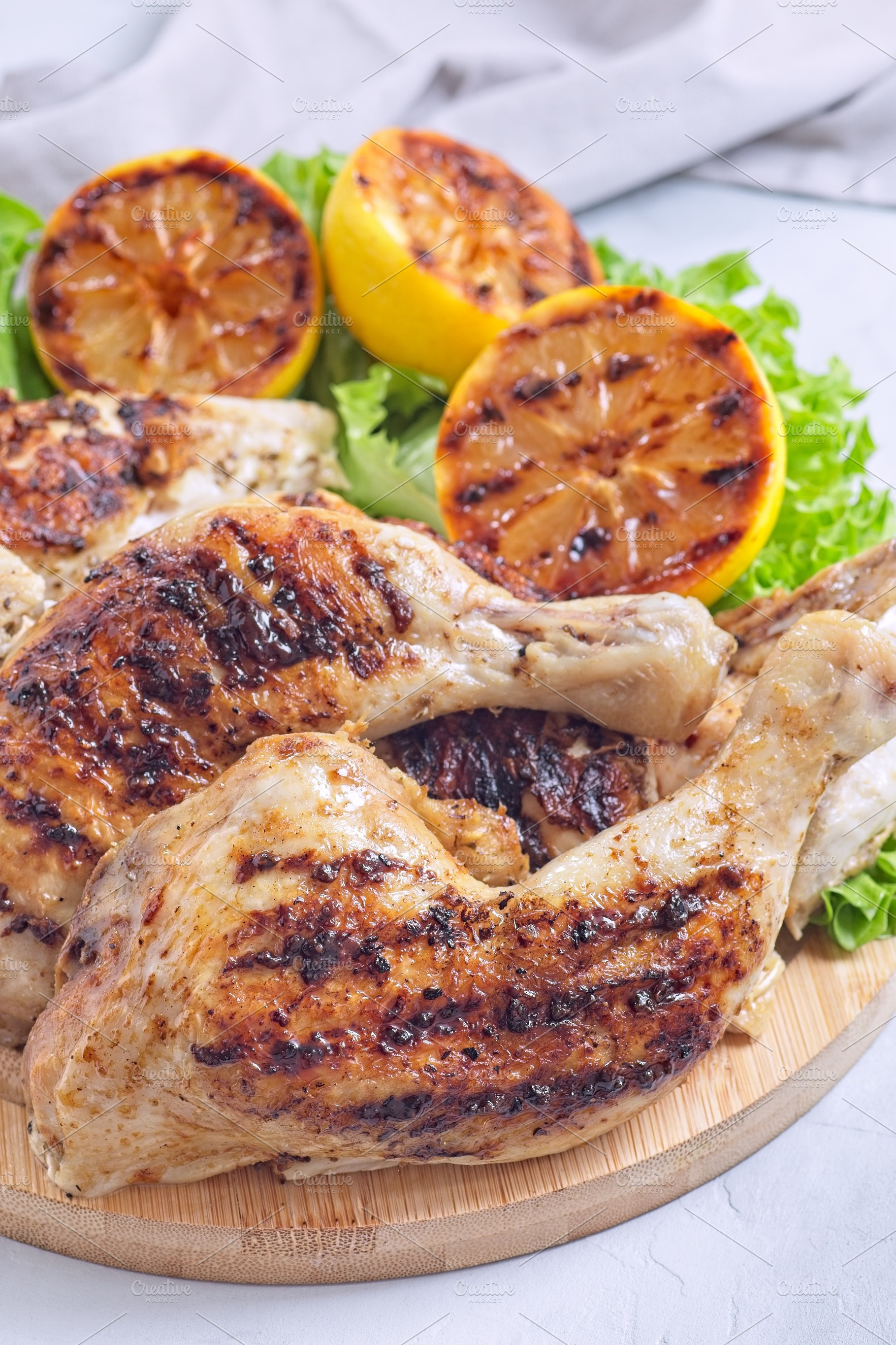 Grilled chicken legs and breast with lemon and lettuce on wooden board, vertica, a Food & Drink Photo by iuliia_n
