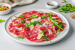 Beef carpaccio served with fresh arugula and shaved cheese on a white plate, a Food & Drink Photo by AlyaAnd