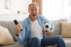 Excited mature man watching tv celebrating goal holding ball, a Photo by Prostock-Studio