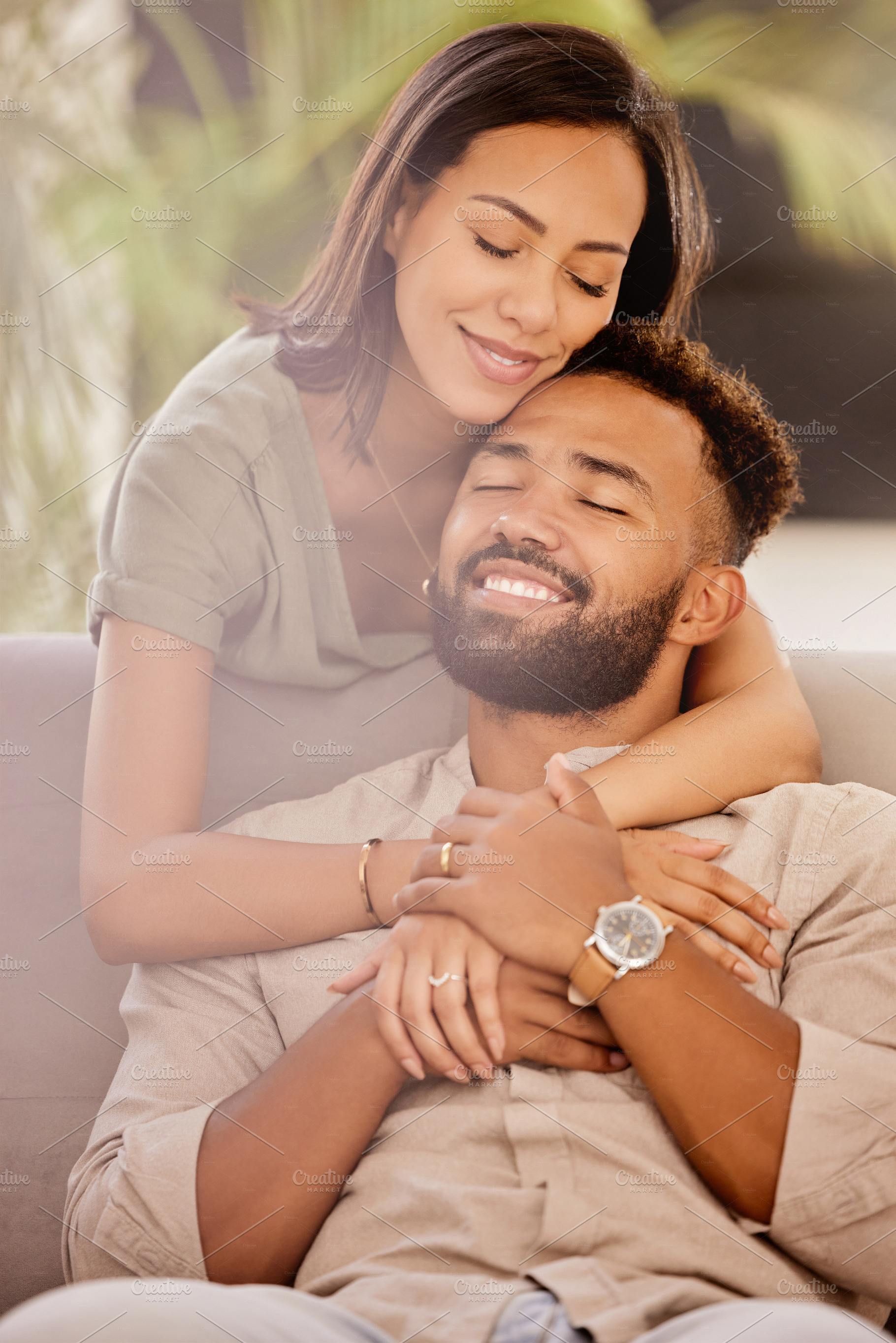 Couple, man and black woman on sofa for hug, love and care in living room to relax while happy. Black man, woman and marriage for romance, embrace and smile together on couch in lounge with happiness, a Photo by Peopleimages.com