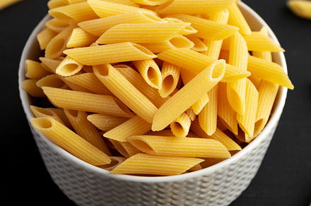 Organic Dry Penne Pasta in a Bowl on a black background, side vi, a Food & Drink Photo by LiudmylaChuhunova
