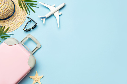 Pink suitcase, airplane model, sunglasses and straw hat on blue