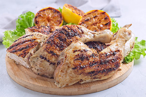 Grilled chicken legs and breast with lemon and lettuce on wooden board, horizon, a Food & Drink Photo by iuliia_n