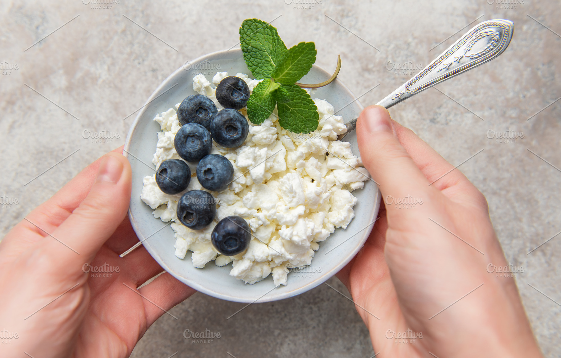Hands holding bowl of cottage cheese, blueberries, mint, a Food & Drink Photo by Olena Rudo