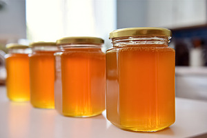 Row of natural honey jars with golden liquid standing on a white, a Photo by Studio ANNA