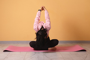 Active woman practicing a seated yoga pose on a pink mat against, a Person Photo by Ales Munt