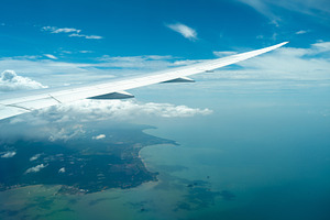 Airplane wing above coastline and clouds in bright sky, a Transportation Photo by GoodGoods