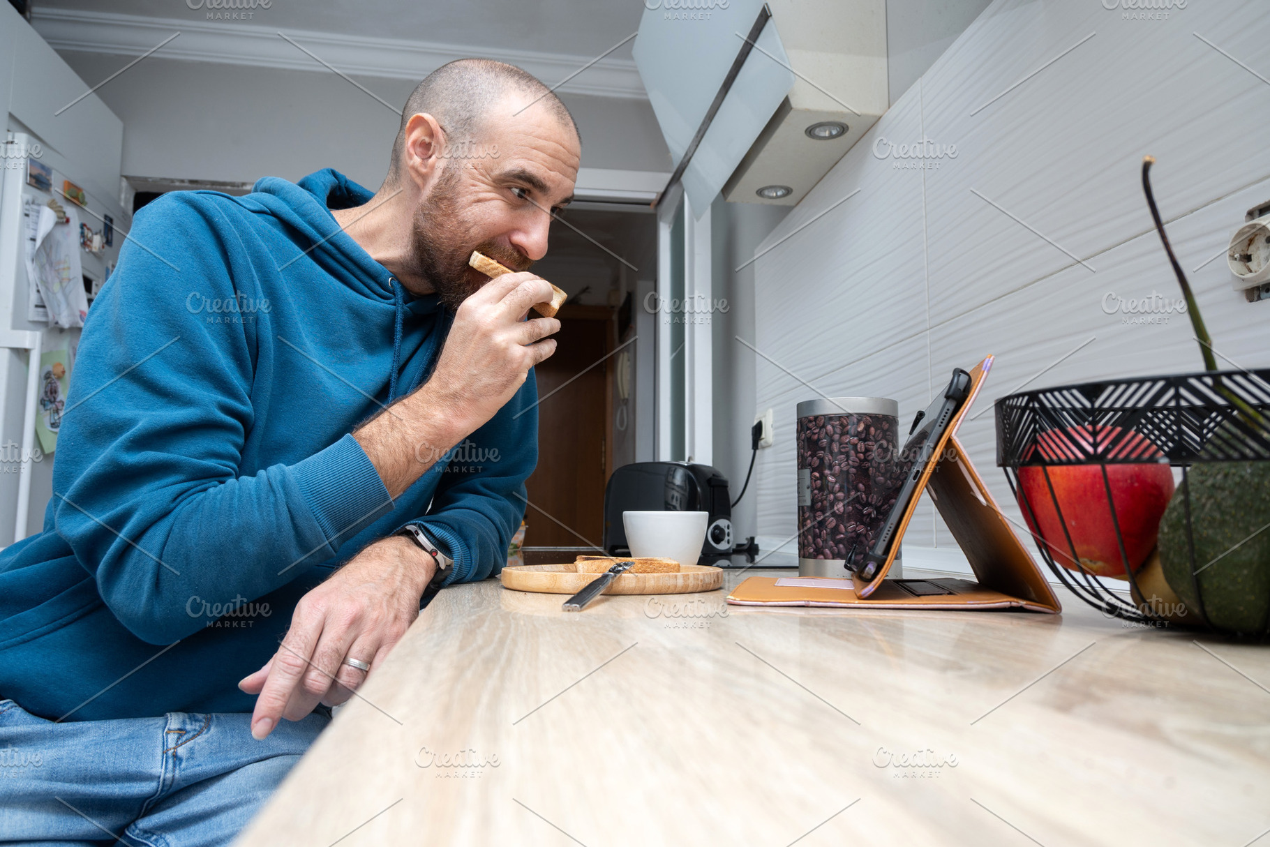 Man having toast for breakfast while using a tablet at home, a Food & Drink Photo by etorres69