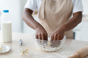 Cropped millennial african american woman in apron making dough on table in kit, a Person Photo by Prostock-Studio